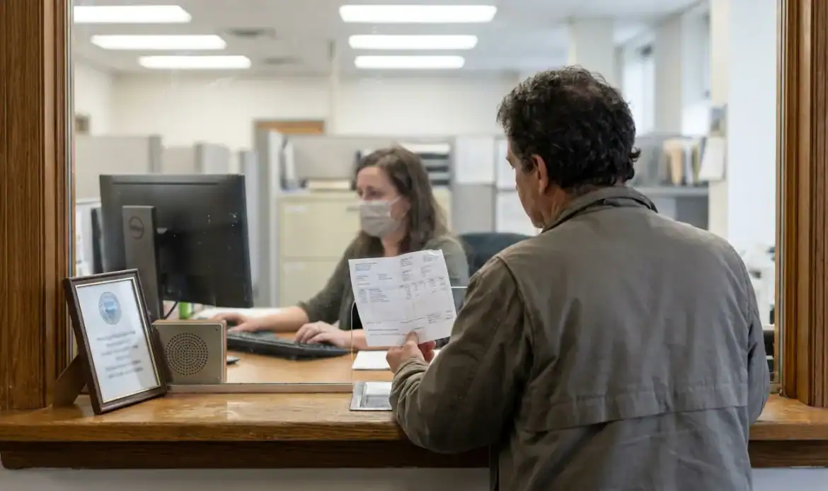 man holding document at government office service window with masked clerk